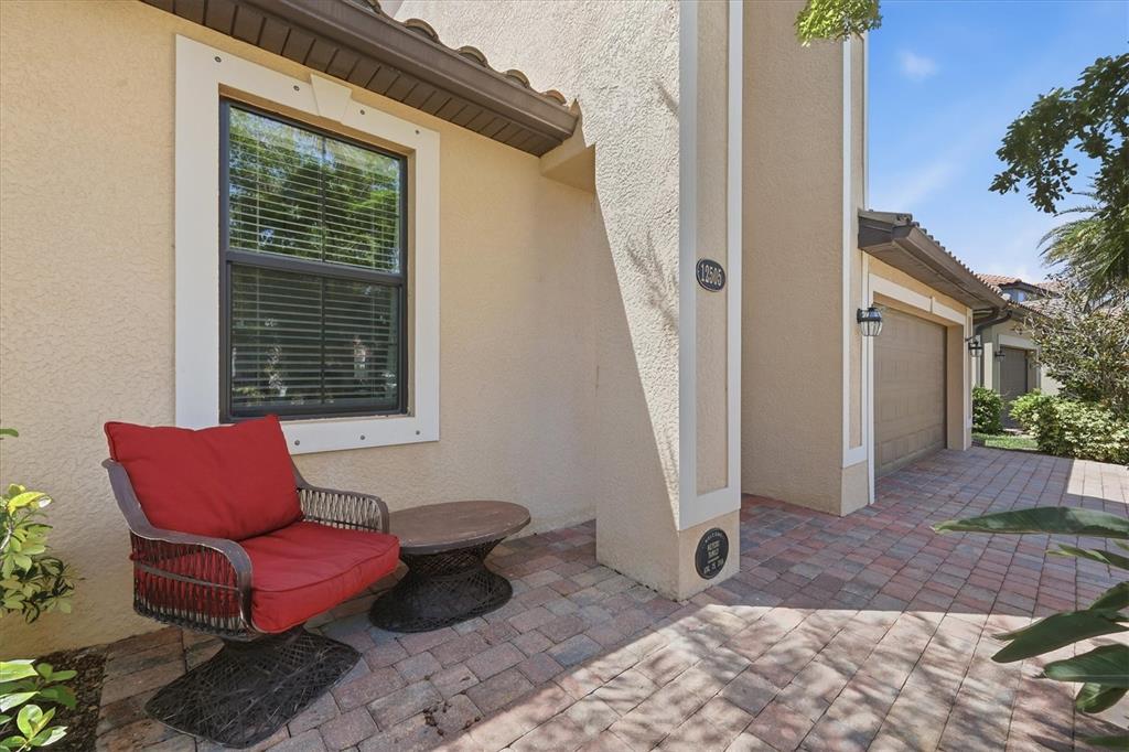 A red chair and small table sit on a paved patio outside a beige house — 12505 CANAVESE LANE, VENICE, FL