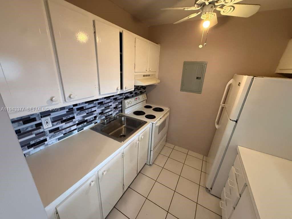 A small kitchen features white cabinets, a tiled backsplash, a white stove, and white appliances — 2916 Funston St # 53A, Hollywood FL 33020, HOLLYWOOD, FL