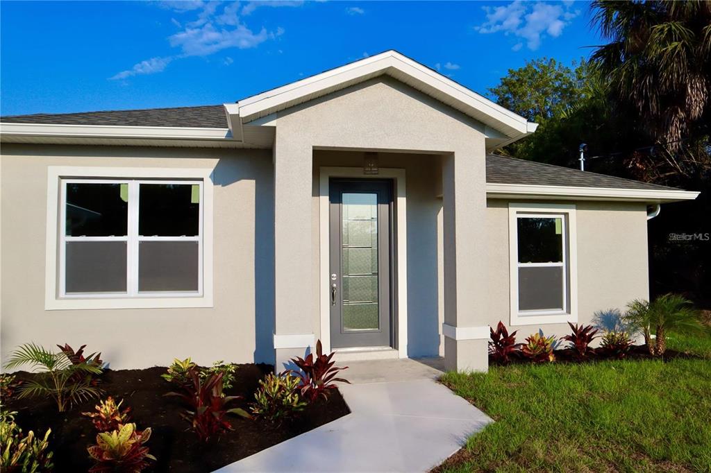 The exterior of a light-colored house features a gray front door and landscaped garden beds — 2957 TOMASO ROAD, NORTH PORT, FL