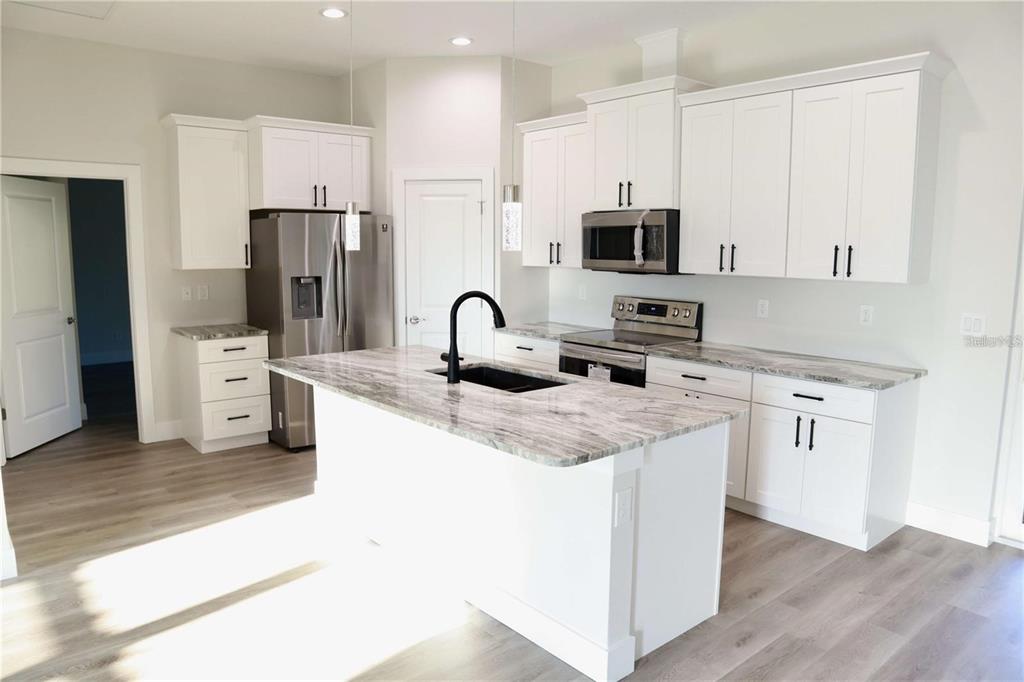 A modern kitchen features white cabinets, a marble-patterned island, stainless steel appliances, and wood flooring — 2957 TOMASO ROAD, NORTH PORT, FL
