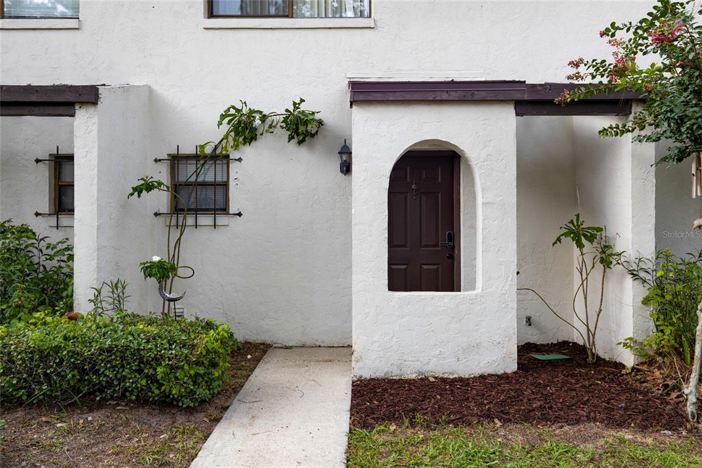 The exterior of a white stucco townhouse features a brown arched door and a small window — 2635 SW 35TH PLACE UNIT 1704, GAINESVILLE, FL