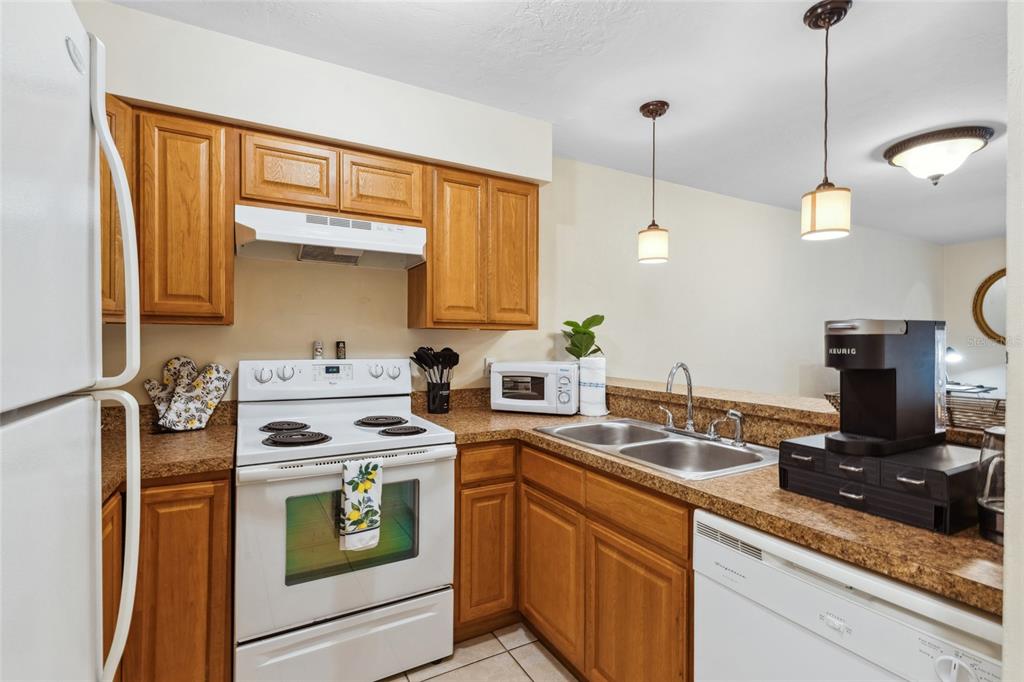 A kitchen with wood cabinets, white appliances, and a double sink with a breakfast bar — 2635 SW 35TH PLACE UNIT 1704, GAINESVILLE, FL