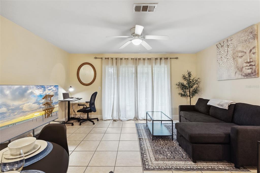A living room features tile flooring, a sectional sofa, a desk, and sliding glass doors — 2635 SW 35TH PLACE UNIT 1704, GAINESVILLE, FL