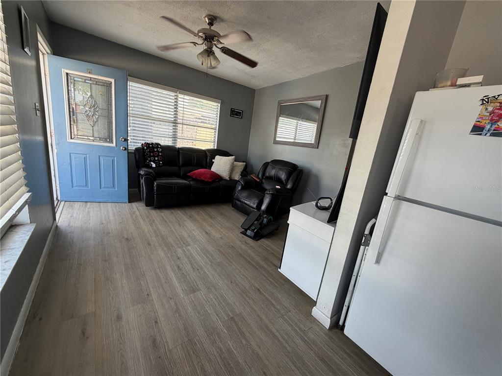 A living room with light wood flooring, a ceiling fan, and an open kitchen view — 2318 W POWHATAN AVENUE, TAMPA, FL