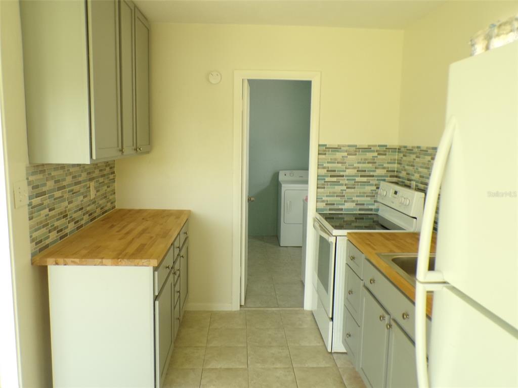 A kitchen features gray cabinets, a wood countertop, a mosaic backsplash, and a laundry room doorway — 4011 GROBE STREET, NORTH PORT, FL