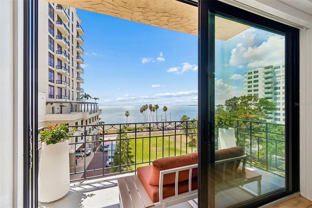 A balcony with outdoor seating overlooks a waterfront view and nearby high-rise buildings — 2109 BAYSHORE BOULEVARD UNIT 504, TAMPA, FL