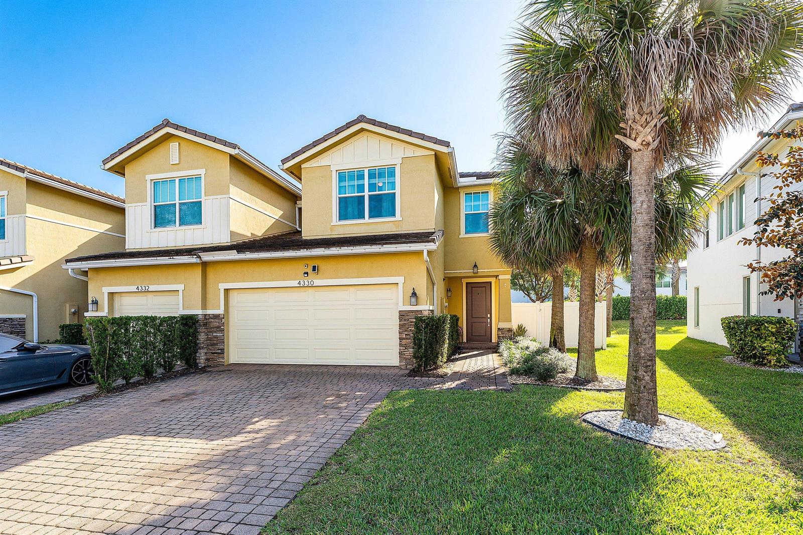 A two-story yellow stucco house with a paved driveway and palm trees at sunset — 4330 Lago Drive, Deerfield Beach FL 33064, DEERFIELD BEACH, FL