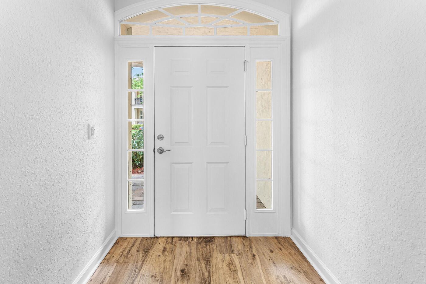 A white front door with sidelights and an arched transom window sits above wood flooring — 8058 Murano Circle, Palm Beach Gardens FL 33418, PALM BEACH GARDENS, FL