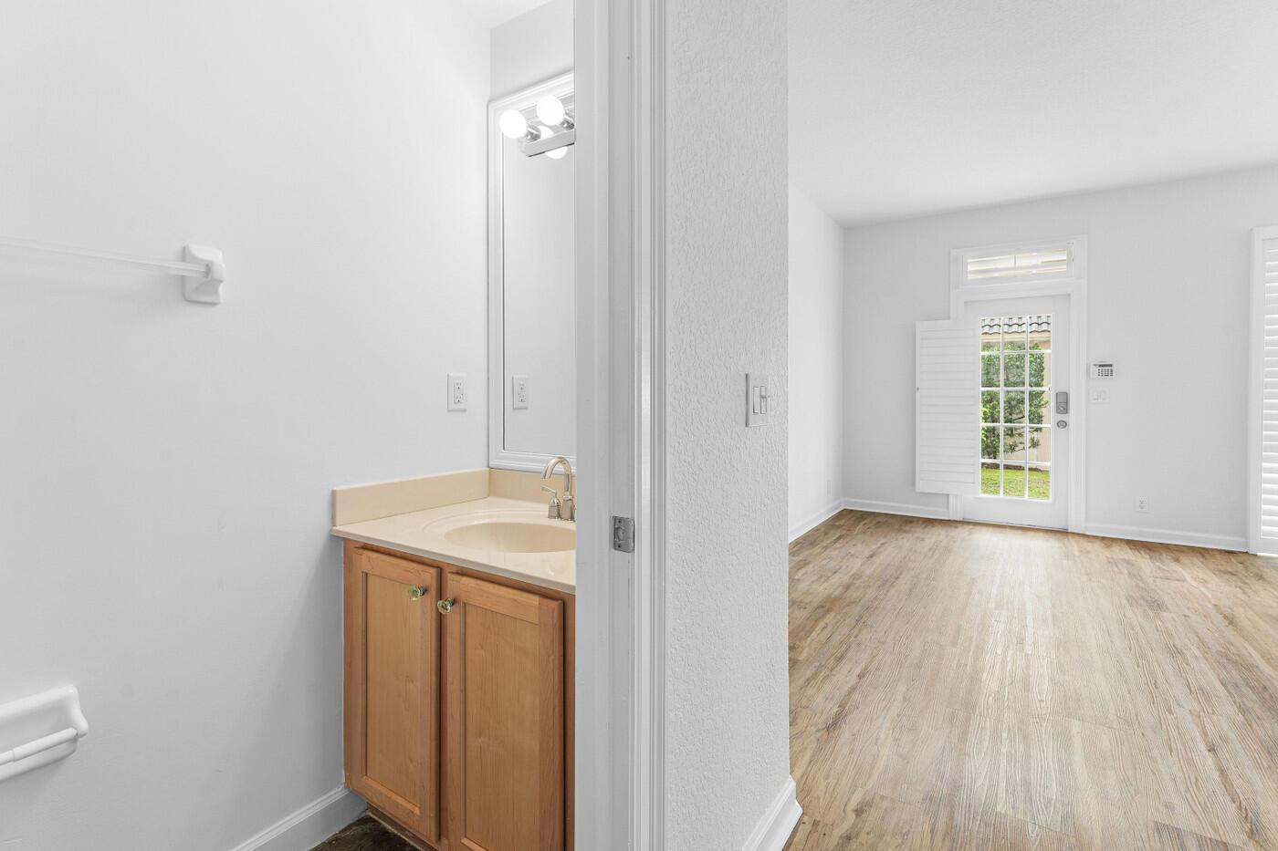 A bathroom vanity with a light wood cabinet sits beside a room with wood flooring — 8058 Murano Circle, Palm Beach Gardens FL 33418, PALM BEACH GARDENS, FL