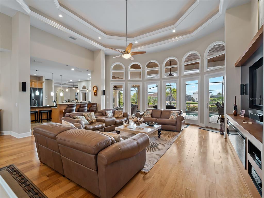 A spacious living room with hardwood floors, leather furniture, and a large arched window wall — 1443 SURFBIRD COURT, PUNTA GORDA, FL