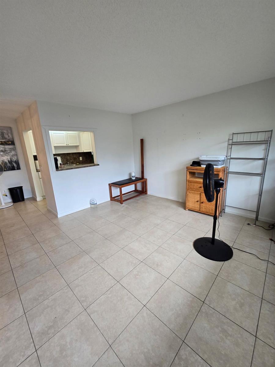 An empty living room with light tile flooring, a kitchen pass-through window, and a ceiling fan — 133 Ventnor I Drive # 133, Deerfield Beach FL 33442, DEERFIELD BEACH, FL