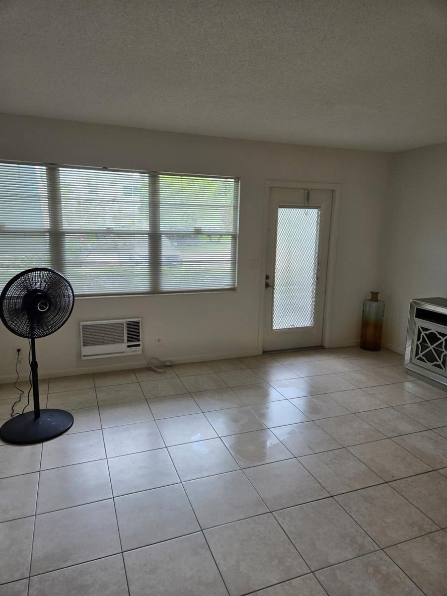 A living room with tile flooring, a window with blinds, a wall air conditioner, and a door — 133 Ventnor I Drive # 133, Deerfield Beach FL 33442, DEERFIELD BEACH, FL