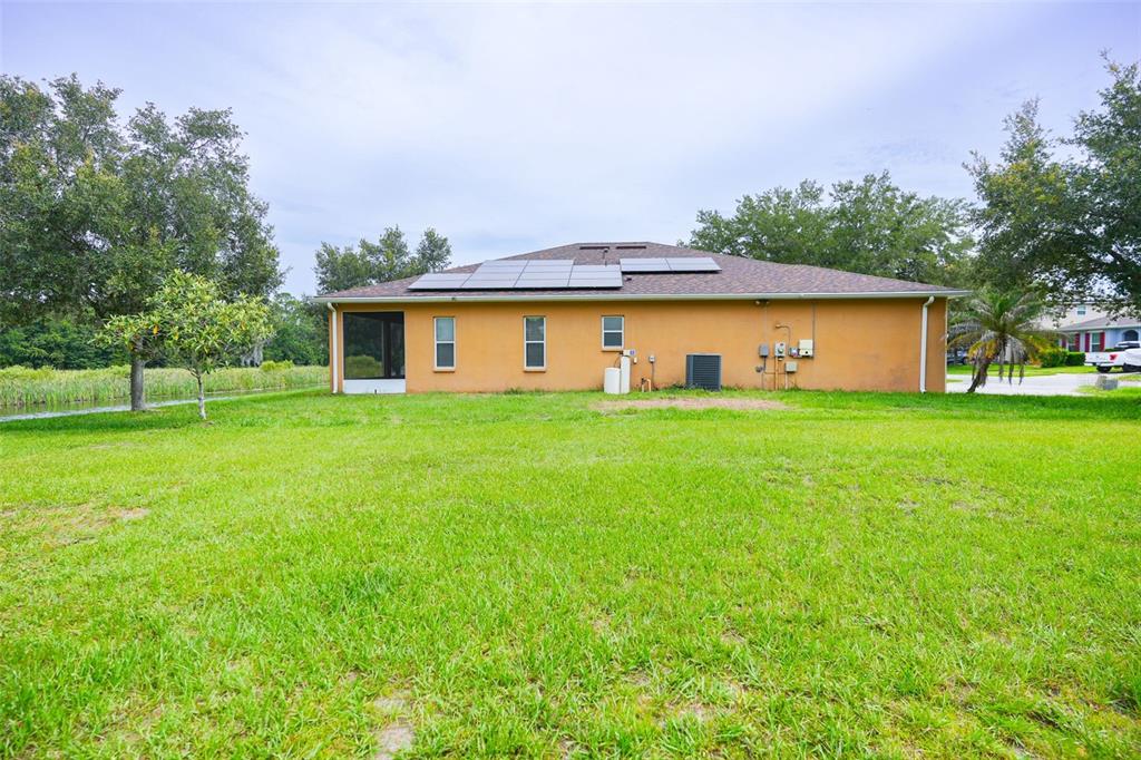 The rear exterior of a single-story house with solar panels and a screened-in porch — 6019 EVANSBROOK DRIVE, ZEPHYRHILLS, FL
