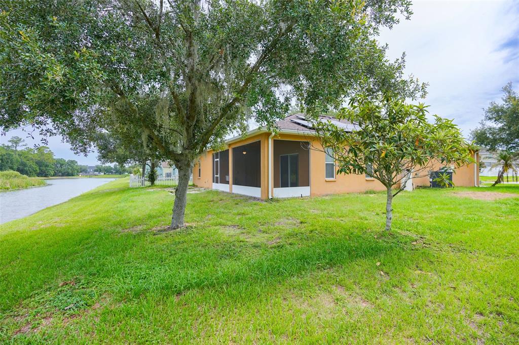The exterior of a tan house with a screened-in porch sits beside a small lake — 6019 EVANSBROOK DRIVE, ZEPHYRHILLS, FL