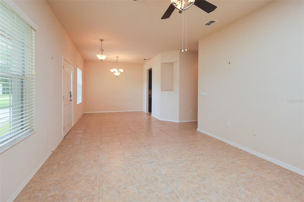 An empty room with tan tile flooring, two light fixtures, and a ceiling fan — 6019 EVANSBROOK DRIVE, ZEPHYRHILLS, FL