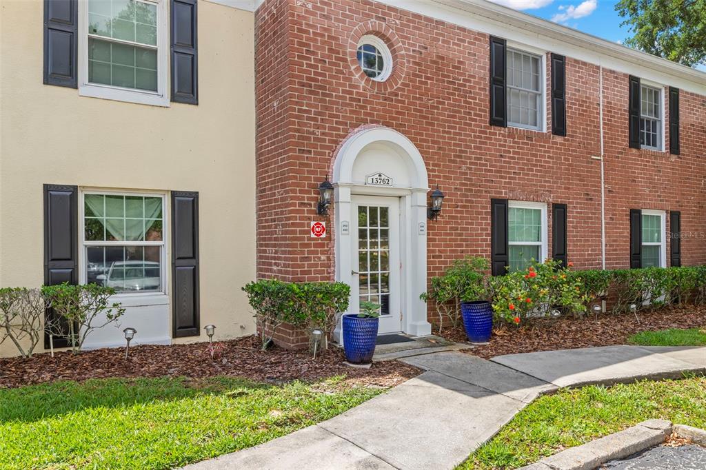 A two-story brick and stucco building exterior features a white front door with shutters — 13762 ORANGE SUNSET DRIVE UNIT 102, TAMPA, FL
