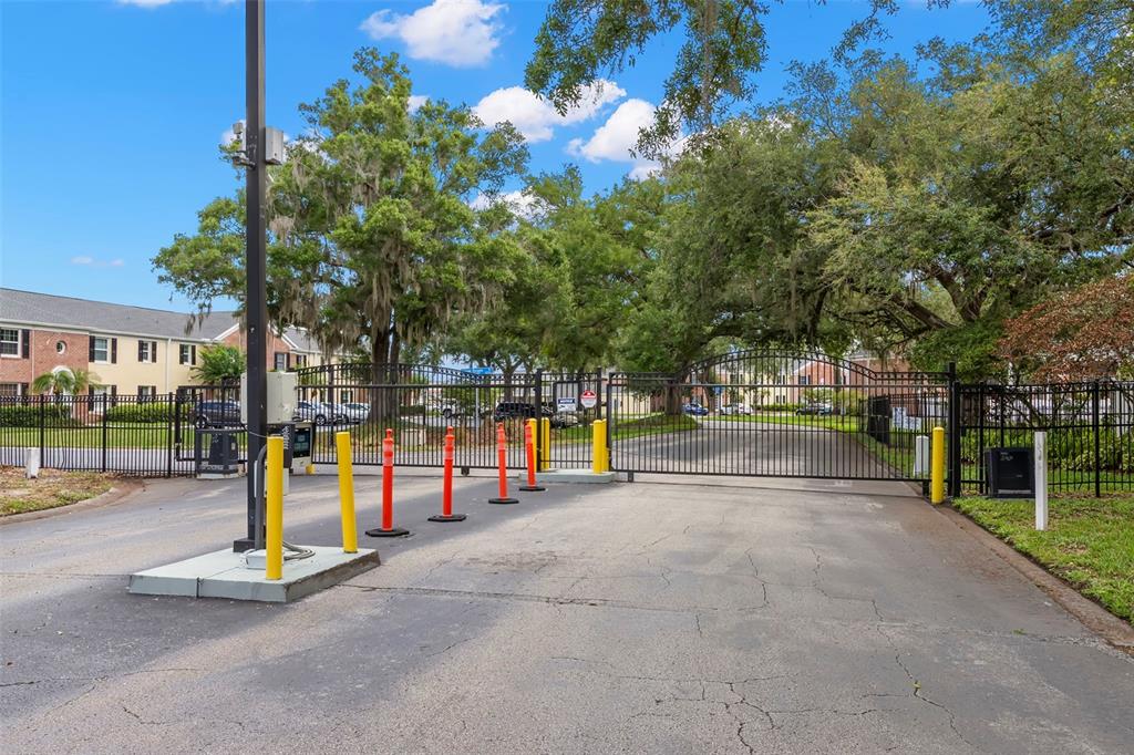 A gated entrance with a black metal fence and traffic bollards leads into a residential complex — 13762 ORANGE SUNSET DRIVE UNIT 102, TAMPA, FL