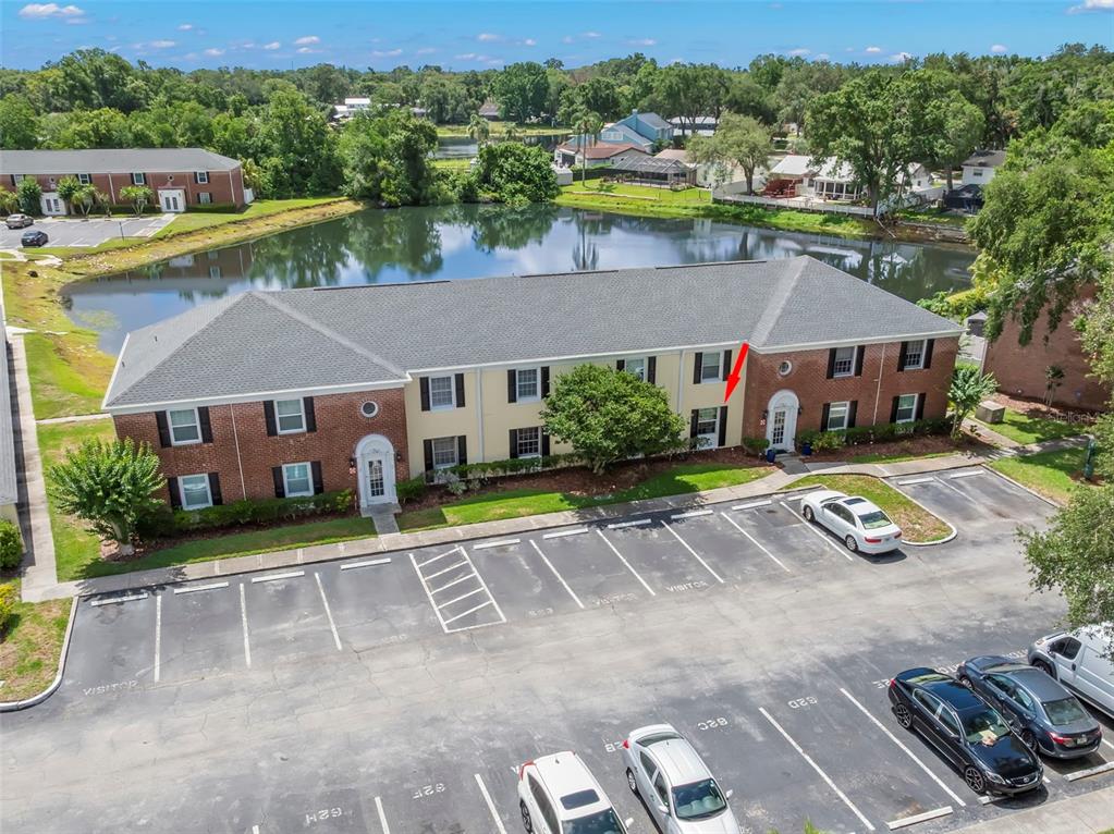 An aerial view of a two-story apartment building with a parking lot and pond — 13762 ORANGE SUNSET DRIVE UNIT 102, TAMPA, FL