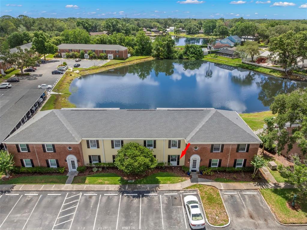 An aerial view shows a two-story brick apartment building situated next to a pond — 13762 ORANGE SUNSET DRIVE UNIT 102, TAMPA, FL