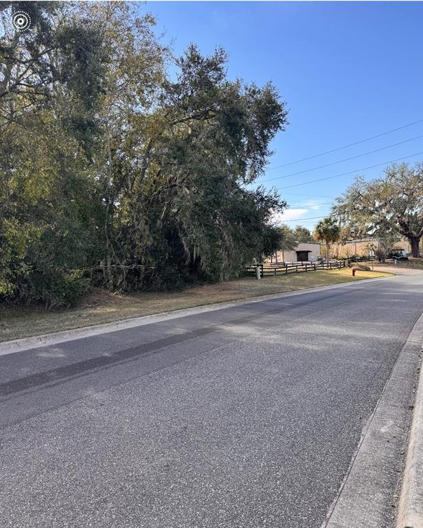 A paved road runs alongside a grassy lot with mature trees and a wooden fence — OAK STREET, LADY LAKE, FL