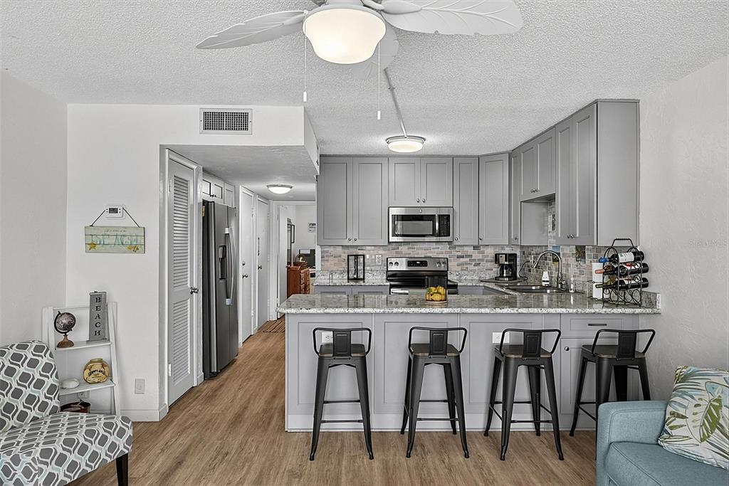 A kitchen features gray cabinets, granite countertops, a breakfast bar with four stools, and wood-look flooring — 1433 N ATLANTIC AVENUE UNIT 329, DAYTONA BEACH, FL