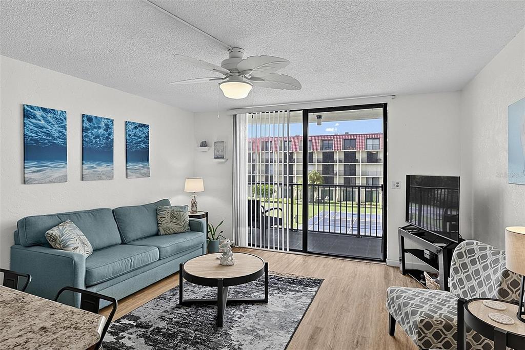 A living room features a blue sofa, patterned armchair, ceiling fan, and a sliding glass door — 1433 N ATLANTIC AVENUE UNIT 329, DAYTONA BEACH, FL