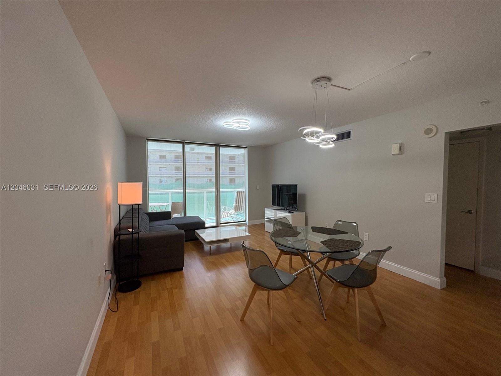 A living and dining area features hardwood floors, a glass table, and a balcony view — MIAMI, FL