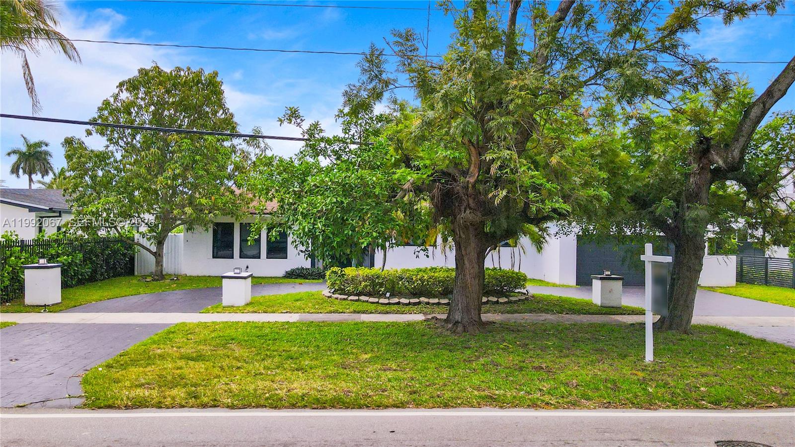 A white single-story house features a circular driveway, mature trees, and a manicured lawn — 1850 NE 199th St, Miami FL 33179, MIAMI, FL