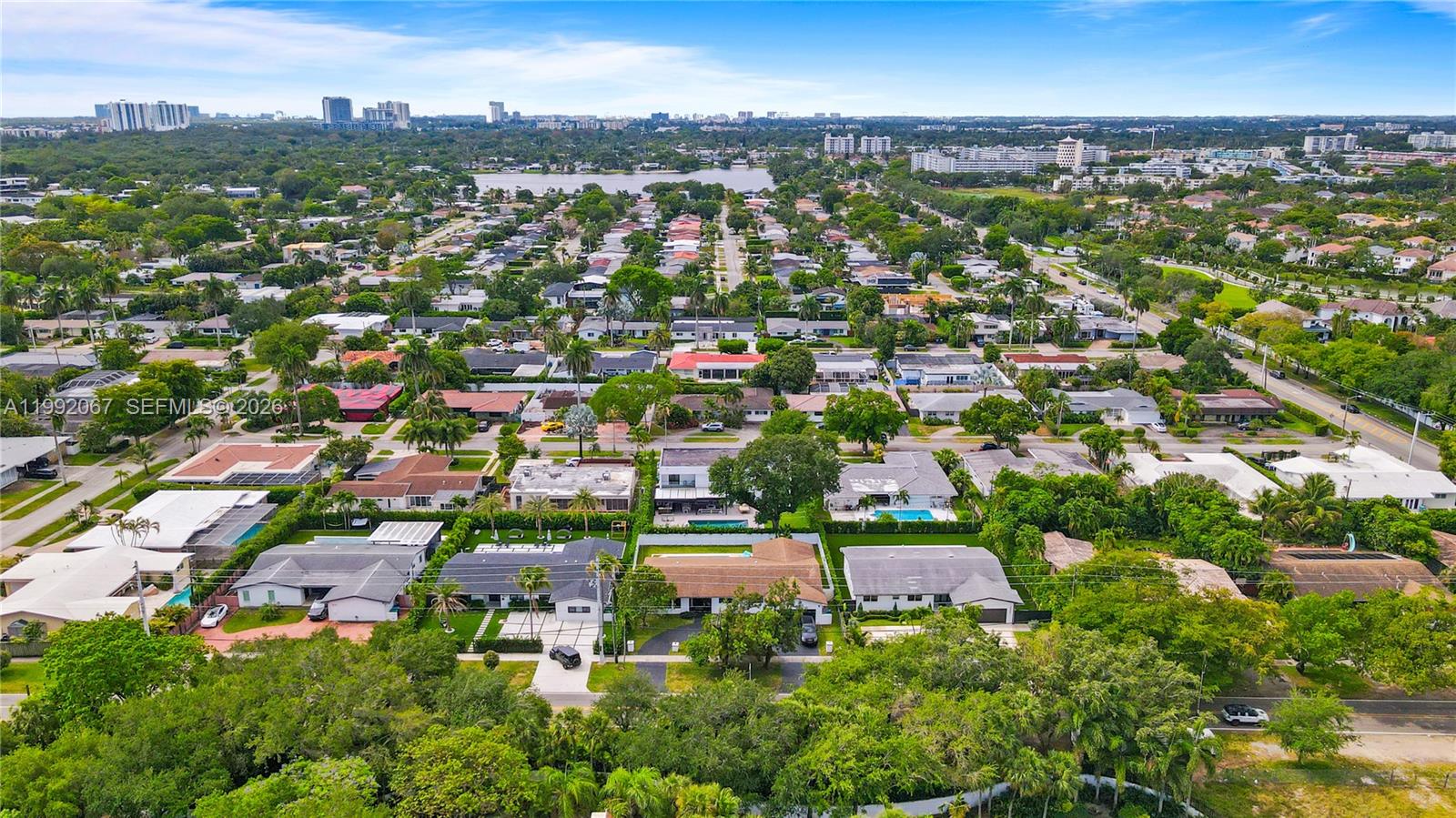 An aerial view shows a residential neighborhood with single-family homes, lush trees, and a lake — 1850 NE 199th St, Miami FL 33179, MIAMI, FL
