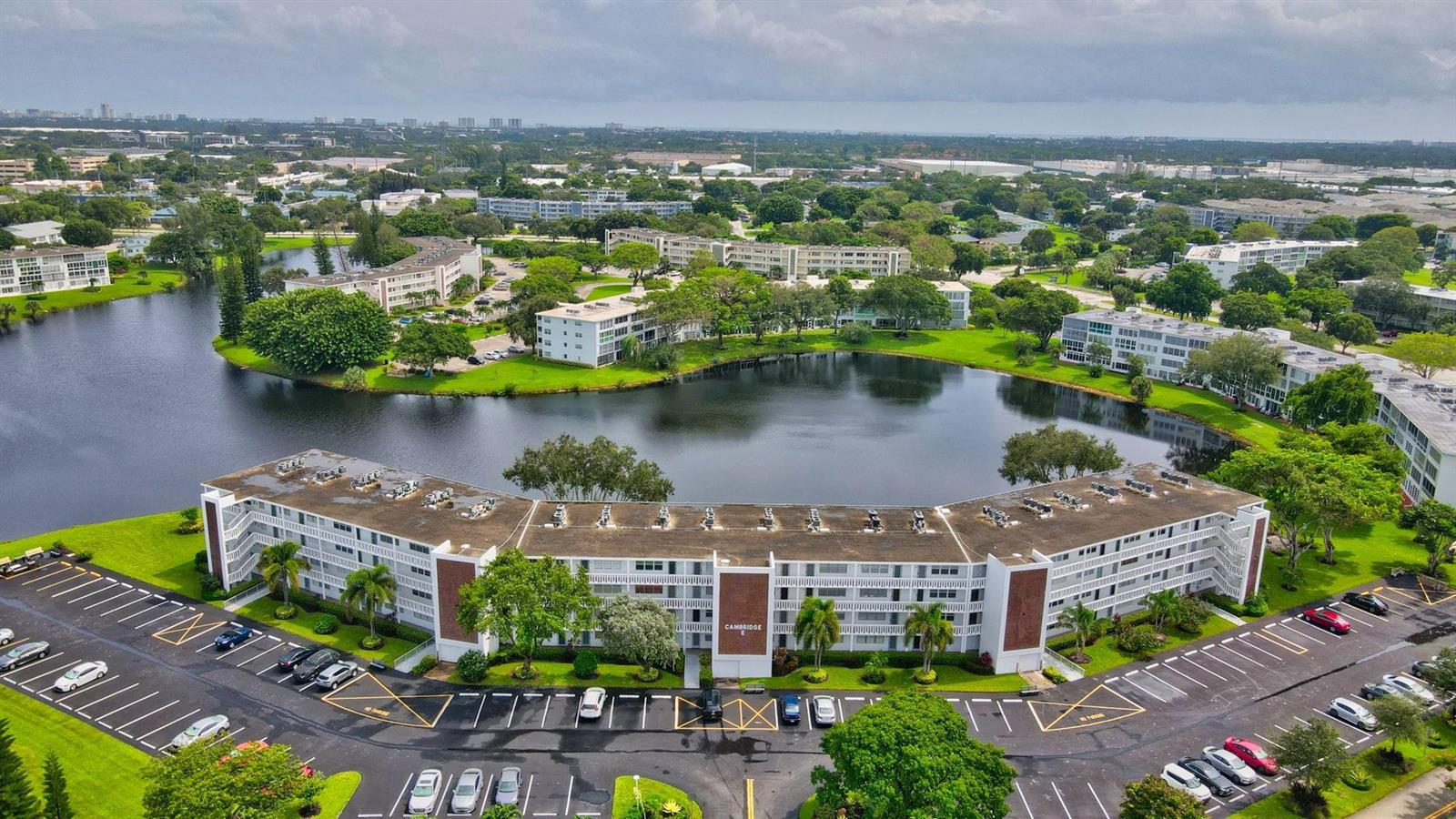 An aerial view shows a multi-story apartment building beside a lake surrounded by green landscaping — 3107 Cambridge # 3107, Deerfield Beach FL 33442, DEERFIELD BEACH, FL