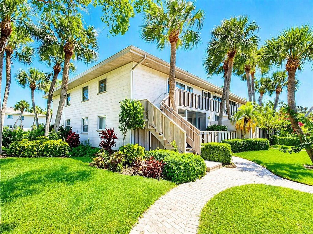 A two-story white building with a wooden staircase and palm trees on a sunny day — 6700 GULF OF MEXICO DRIVE UNIT 143, LONGBOAT KEY, FL