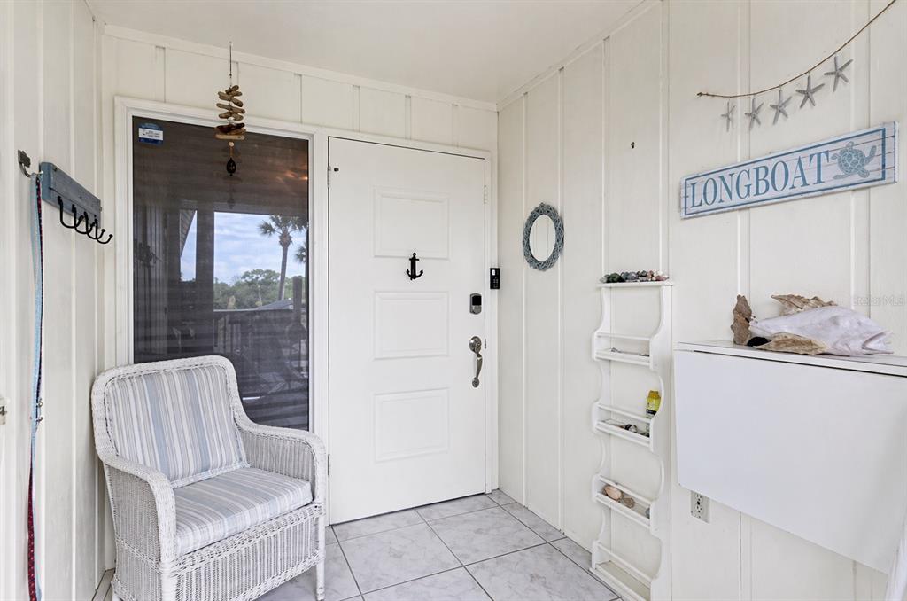 A white-walled entryway features a wicker chair, a front door with an anchor, and decor — 6700 GULF OF MEXICO DRIVE UNIT 143, LONGBOAT KEY, FL