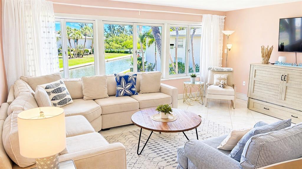 A living room features a beige sectional sofa, a round wooden coffee table, and windows — 6700 GULF OF MEXICO DRIVE UNIT 143, LONGBOAT KEY, FL