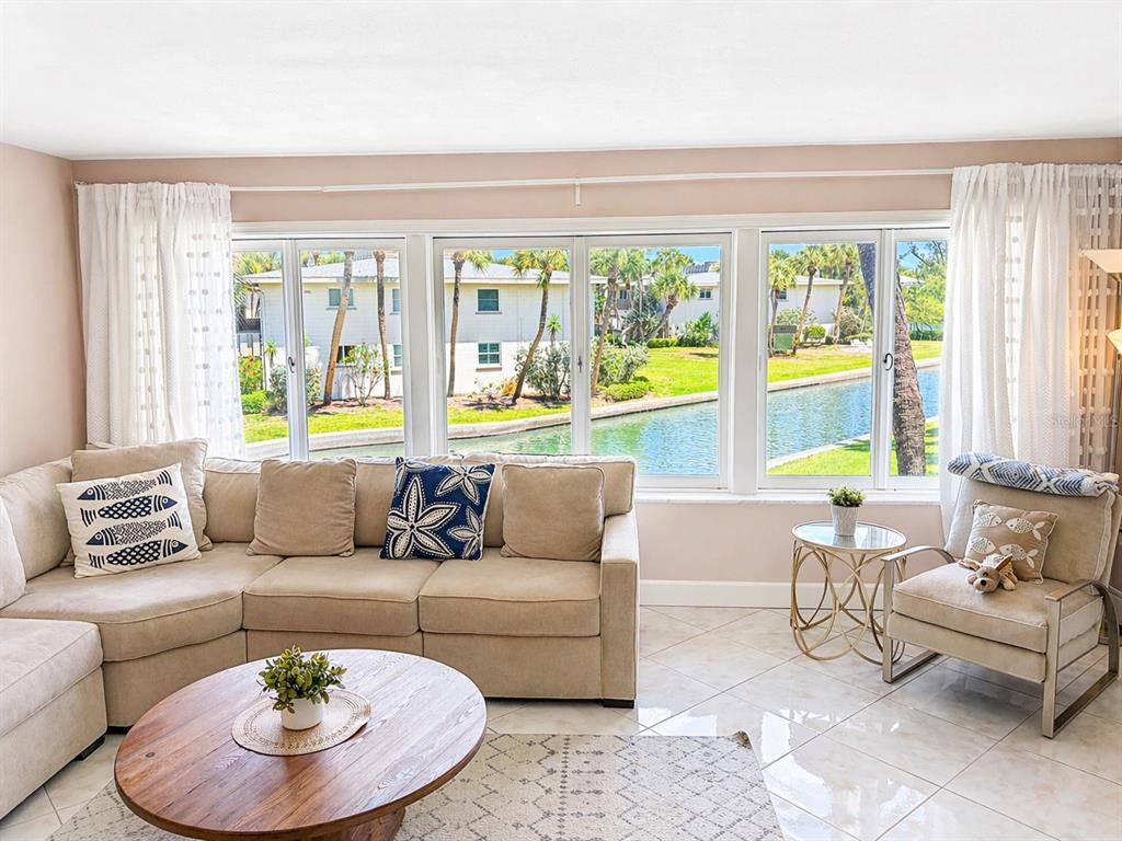 A living room features a beige sectional sofa, a round wooden coffee table, and large windows overlooking a canal — 6700 GULF OF MEXICO DRIVE UNIT 143, LONGBOAT KEY, FL