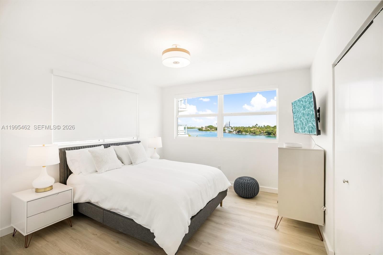 A bright bedroom features a queen bed, white furniture, light wood floors, and a water view — 9881 E Bay Harbor Dr # 504, Bay Harbor Islands FL 33154, BAY HARBOR ISLANDS, FL