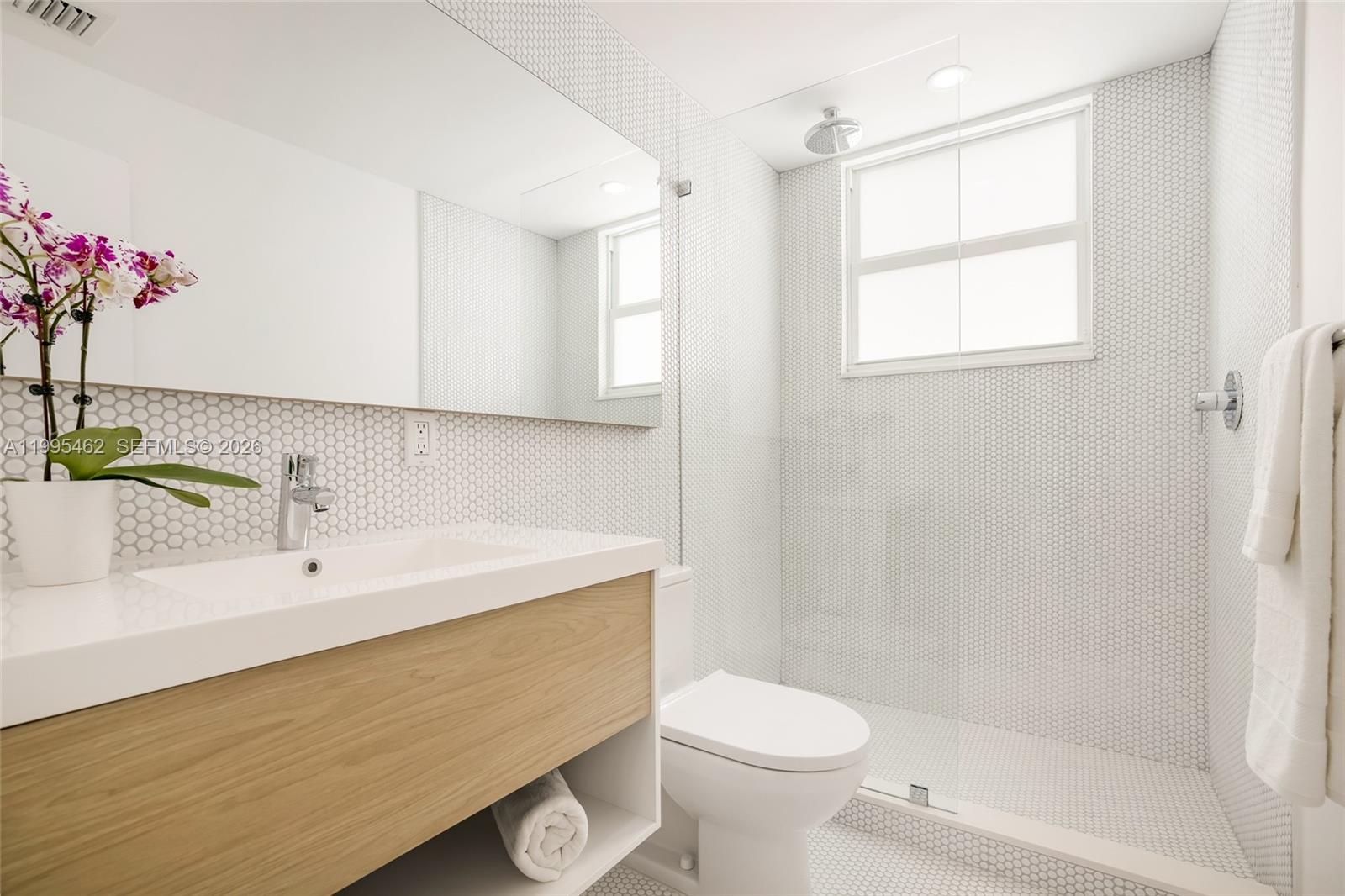 A modern bathroom features a wood vanity, white penny tile walls, and a glass-enclosed shower — 9881 E Bay Harbor Dr # 504, Bay Harbor Islands FL 33154, BAY HARBOR ISLANDS, FL