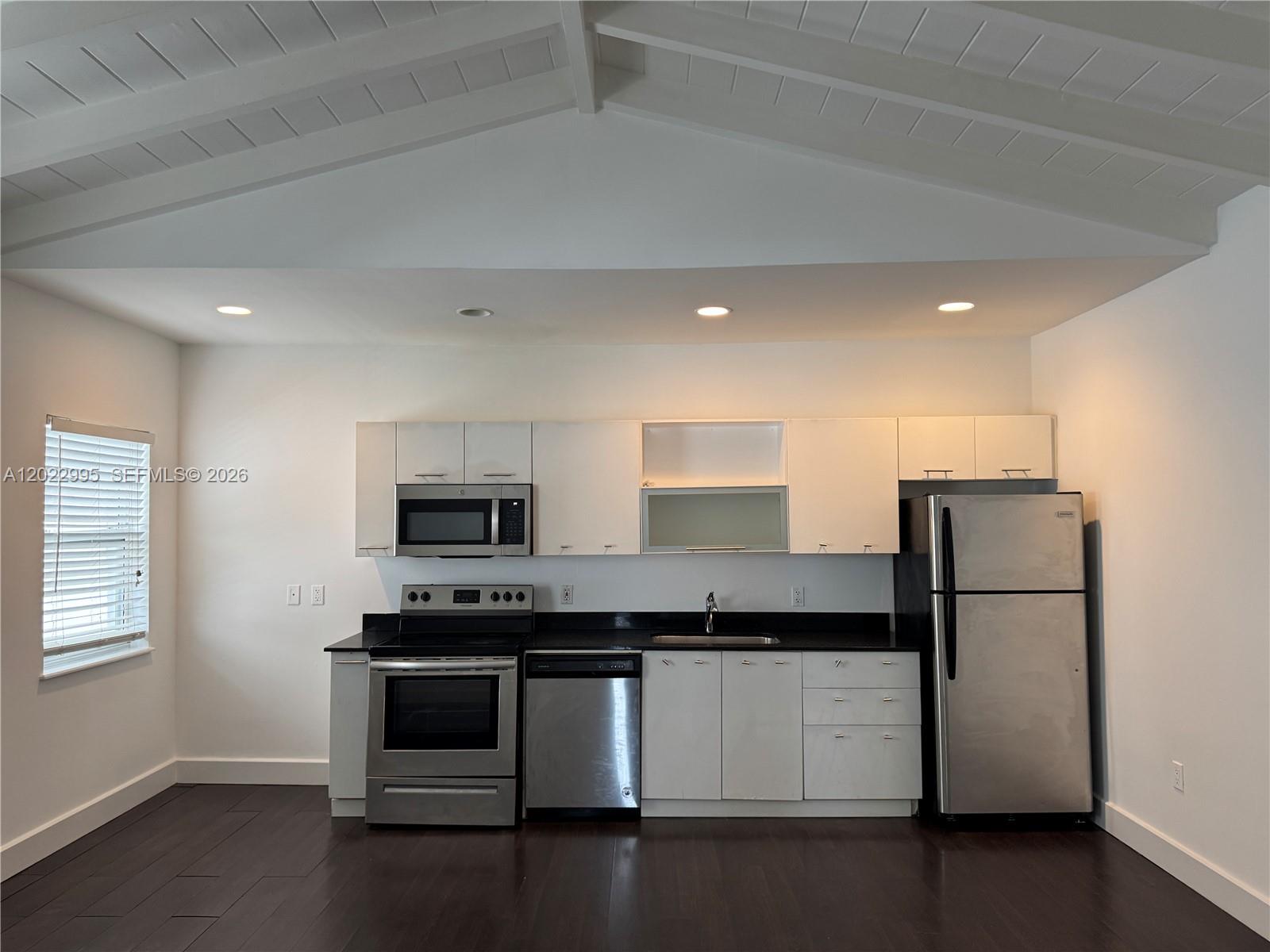 A kitchen features white cabinets, stainless steel appliances, dark countertops, and dark wood flooring — 7734 Abbott Ave # 206, Miami Beach FL 33141, MIAMI BEACH, FL
