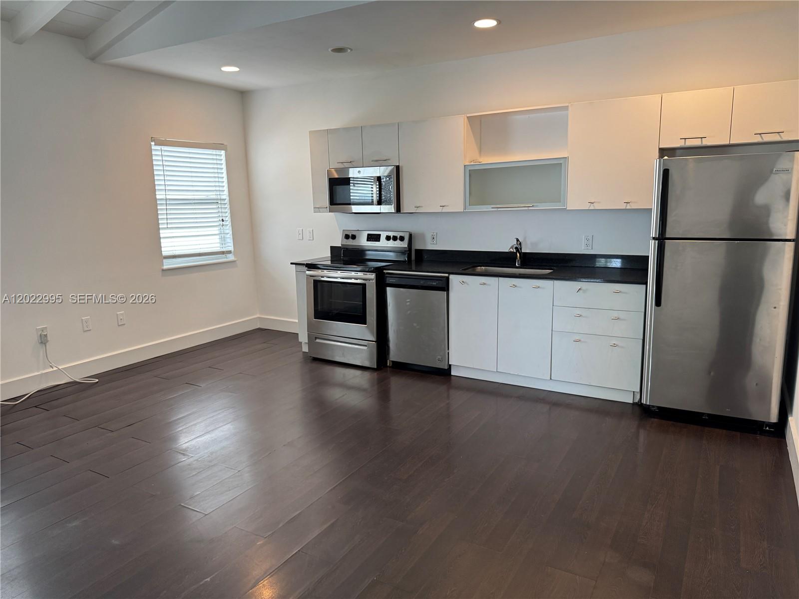 A kitchen features white cabinets, stainless steel appliances, dark countertops, and dark wood flooring — 7734 Abbott Ave # 206, Miami Beach FL 33141, MIAMI BEACH, FL