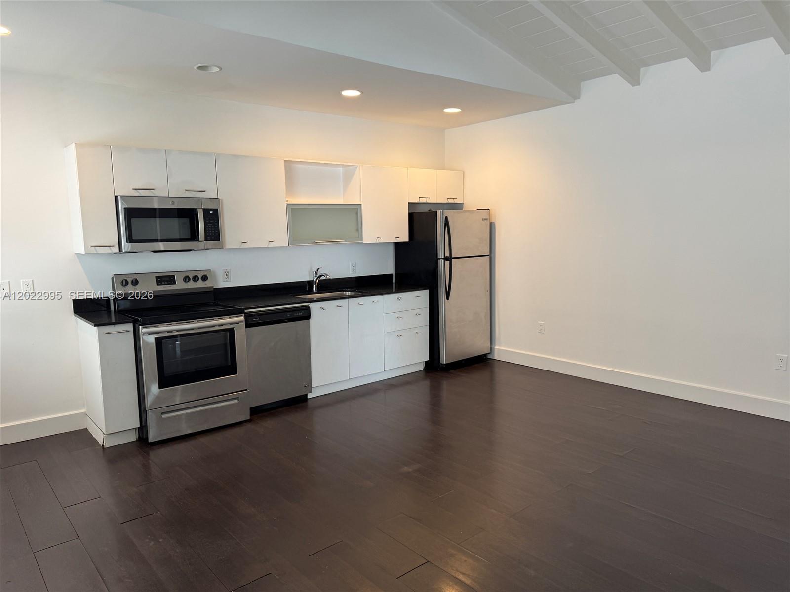 A kitchen with white cabinets, stainless steel appliances, black countertops, and dark wood flooring — 7734 Abbott Ave # 206, Miami Beach FL 33141, MIAMI BEACH, FL