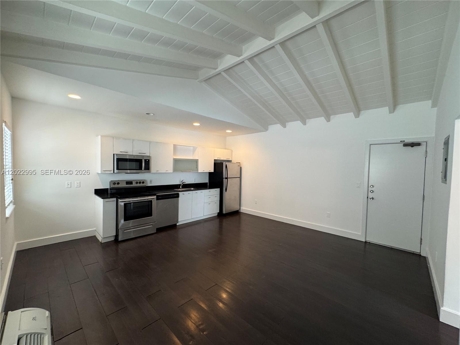 An open-concept kitchen features white cabinets, stainless steel appliances, and dark wood flooring — 7734 Abbott Ave # 206, Miami Beach FL 33141, MIAMI BEACH, FL