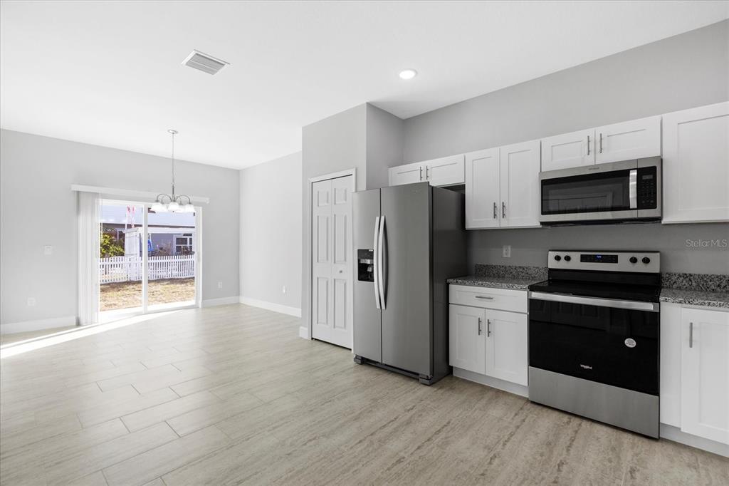 A kitchen with white cabinets, stainless steel appliances, and tile flooring opens to a dining area — 16 TROUT WAY UNIT A & B, POINCIANA, FL