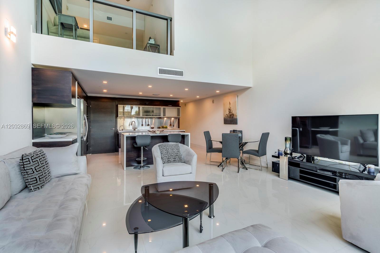 A modern open-concept living room features a kitchen with an island and a lofted balcony — 6000 Collins Ave # 346, Miami Beach FL 33140, MIAMI BEACH, FL