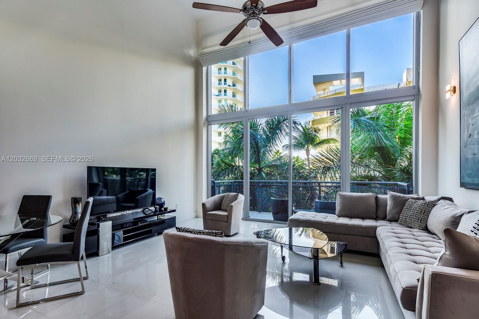 A living room features a high ceiling, floor-to-ceiling windows, and a large sectional sofa — 6000 Collins Ave # 346, Miami Beach FL 33140, MIAMI BEACH, FL
