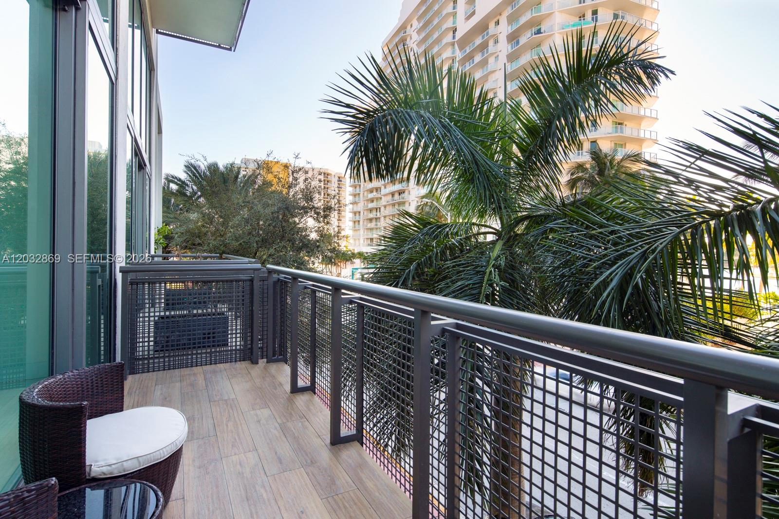 A balcony with wood-look tile flooring, a dark metal railing, and a view of palm trees — 6000 Collins Ave # 346, Miami Beach FL 33140, MIAMI BEACH, FL