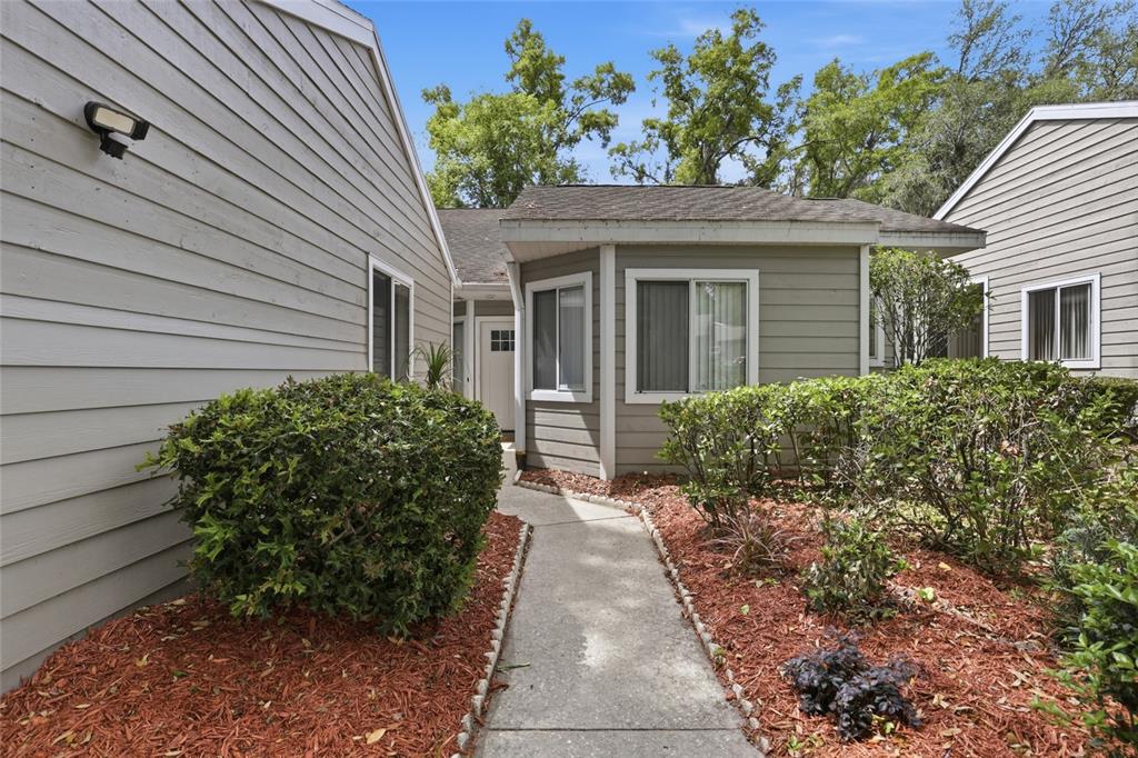 A concrete walkway leads to the front entrance of a gray-sided house with landscaping — 829 NW 124TH DRIVE, NEWBERRY, FL