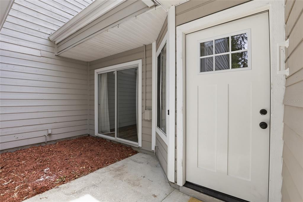 A concrete patio features a sliding glass door and a white front door with windows — 829 NW 124TH DRIVE, NEWBERRY, FL