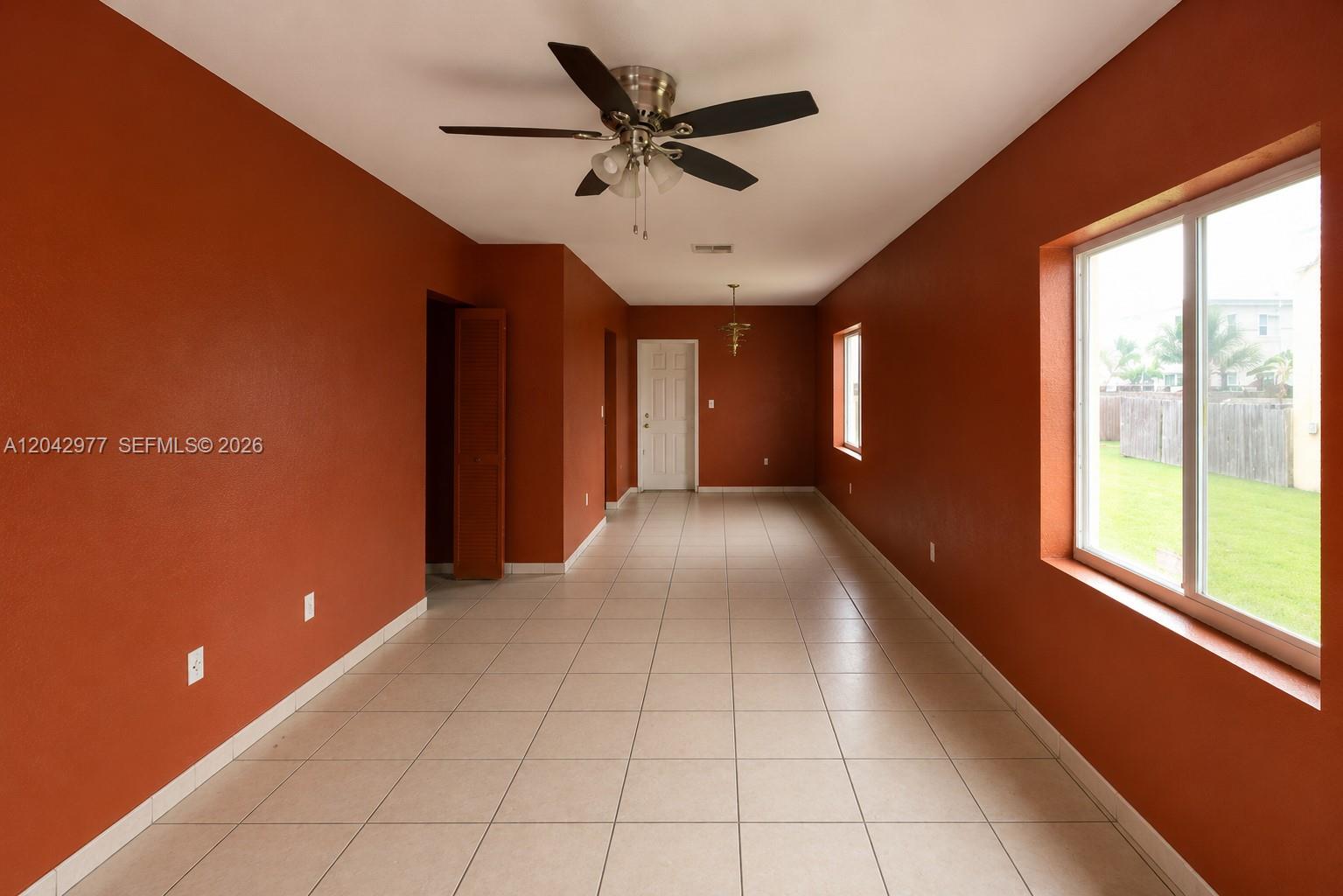 An empty room with terracotta walls, tile flooring, a ceiling fan, and a large window — 420 NW 84th Ter # 420, Miami FL 33150, MIAMI, FL
