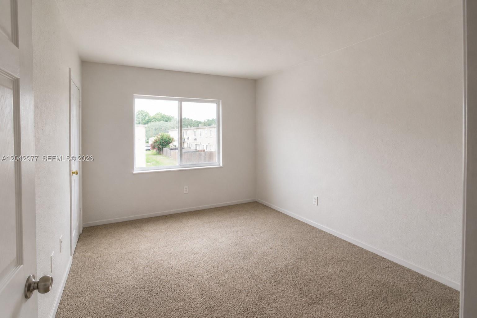 An empty bedroom features beige carpeting, white walls, and a window overlooking a residential area — 420 NW 84th Ter # 420, Miami FL 33150, MIAMI, FL