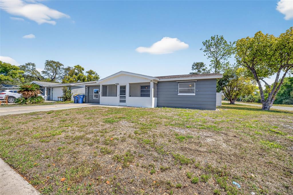 A single-story house with a gray exterior, a screened-in front porch, and a large yard — 1012 PRESCOTT LANE, HOLIDAY, FL