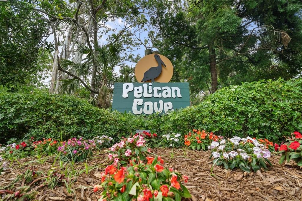 A sign for Pelican Cove sits in a garden bed filled with colorful flowers — 1711 PELICAN COVE ROAD UNIT 341, SARASOTA, FL
